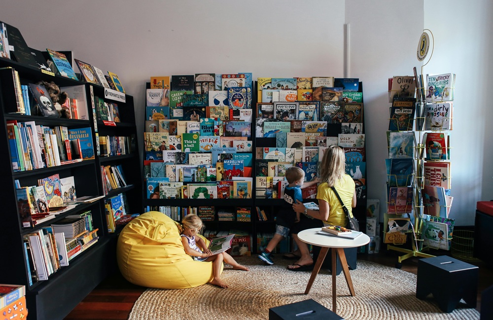 Children and a parent exploring books in a cozy local bookstore, symbolizing community literacy programs and small business contributions in Seattle.